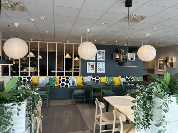 Matplats i IKEA Malmös personalmatsal med lång sittbänk, stolar i gröna toner, hängande lampor och växter som ramar in ytan för gemensamma måltider.