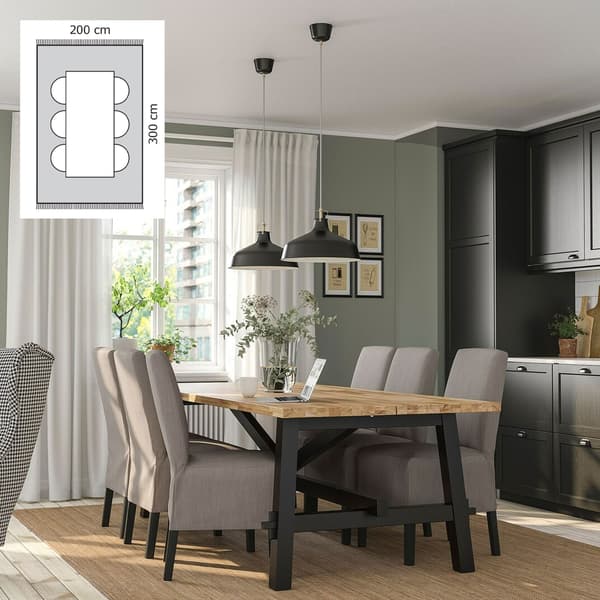 Matrum med träbord och sex stolar på beige matta, svarta lampor ovanför, grönt väggparti med tavlor och i vänstra hörnet en inklippt ritning på en matplats med mått 200×300 cm på mattan.