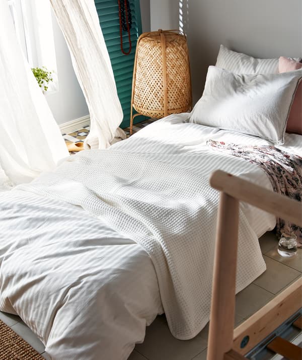 Mattress for sleeping on the floor beside an open window; the corner of a bed frame, suggesting that this is a temporary arrangement.