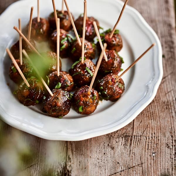 Meatballs served with toothpicks are on a white plate.