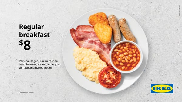 Medium breakfast. White plate on concrete background with scrambled egg, 2 sausages, 1 hash brown, bacon, fried tomato, and small bowl of baked beans