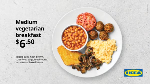 Medium breakfast. White plate on concrete background with scrambled egg, 4 plantballs, fried mushrooms, 1 hash brown, bacon, fried tomato, and small bowl of baked beans, for $6.50