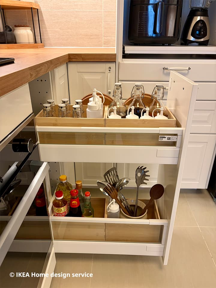 Medium shot of pull-out drawer filled with sauce bottles and kitchen utensils and kitchen accessories in IKEA METOD kitchen drawer.