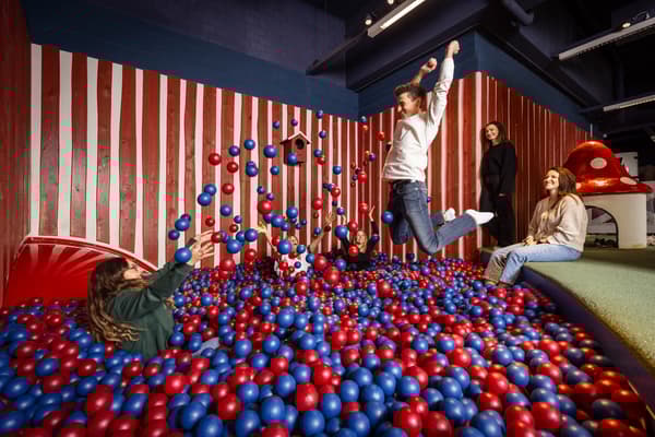 Mehrere Personen sind im Bällebad, eine Person springt rein, eine andere wirft blaue und rote Bälle in die Luft.