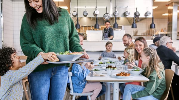 Mehrere Personen sitzen am Tisch in einem IKEA Einrichtunghaus, im Vordergrund nimmt sich ein Kind etwas von dem Teller einer Frau.
