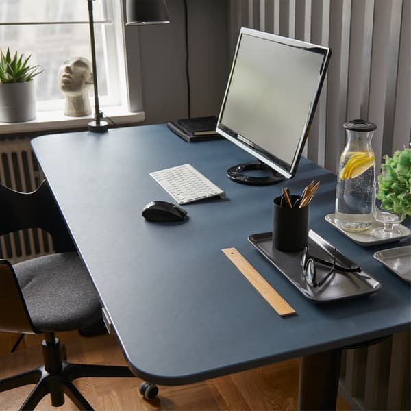 Meja duduk/berdiri BEKANT linoleum berwarna biru/hitam yang ergonomik dengan skrin komputer, botol air dan gelas serta pelbagai item pejabat.