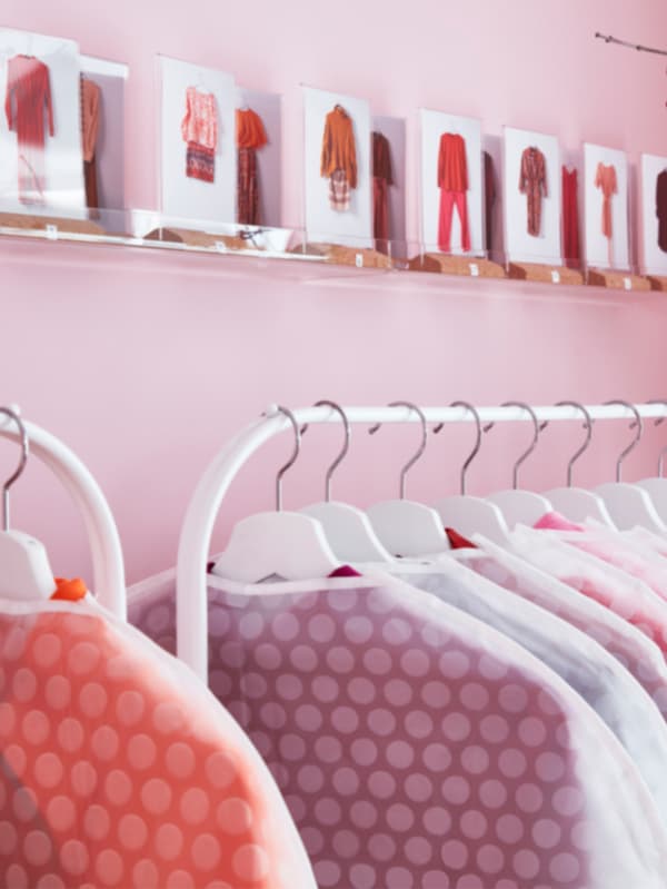 MELLÖSA transparent picture ledges decorated with images of fashionable outfits above clothes hanging on racks.