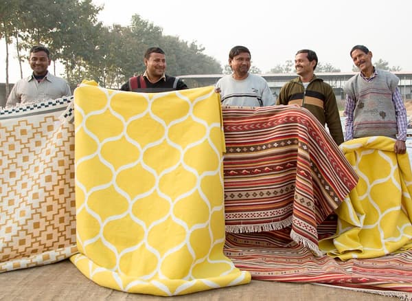Men holding a selection of hand-woven rugs.