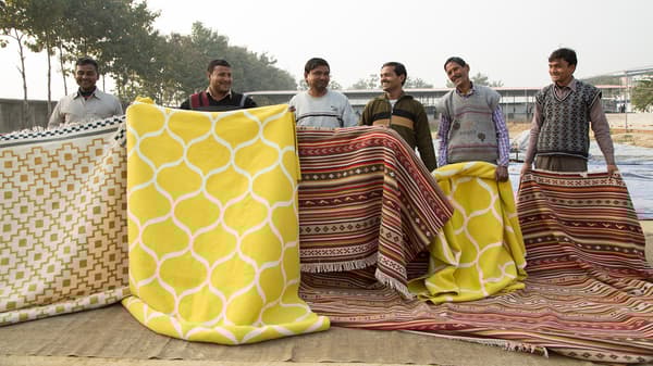 Men holding a selection of hand-woven rugs.