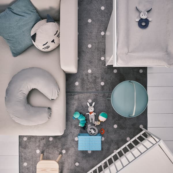 Méridienne beige avec coussins, table à langer et lit bébé SMÅGÖRA en blanc, et tabouret enfant FLISAT sur un tapis gris.