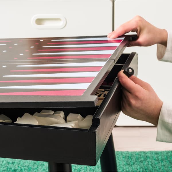 Mesa auxiliar cun taboleiro de backgammon pintado na parte superior. Mans abrindo a parte superior e deixando ver diferentes xogos gardados.