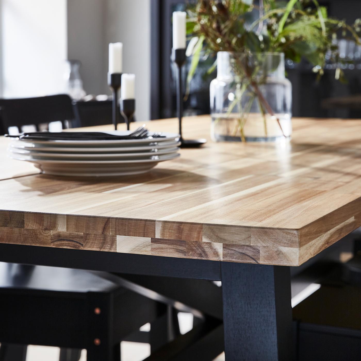 Mesa de comedor de madera con platos, cubiertos, portavelas y un florero encima.
