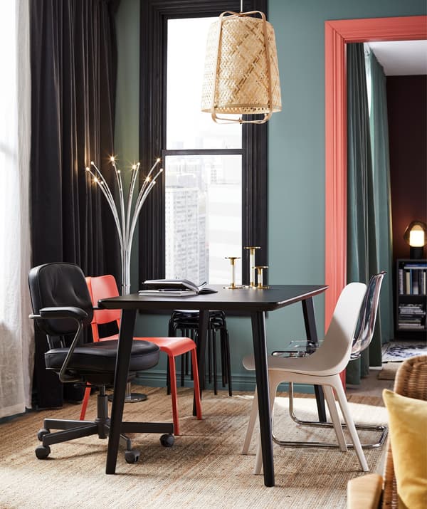 Mesa de refeição na sala com cadeiras todas diferentes. Palete de cores fortes e apontamentos coloridos; iluminação decorativa.