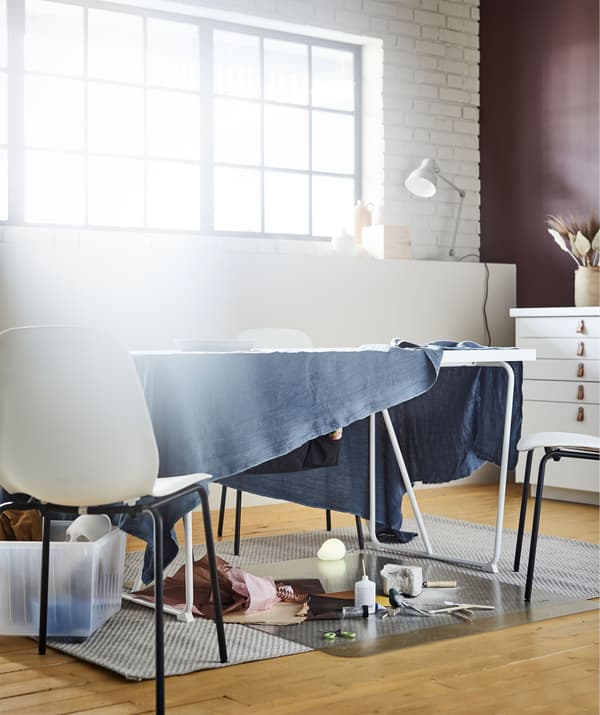Mesa de sala de estar, da que sobresaen varios tecidos, convertida nun lugar de traballo improvisado para pintar ou facer tarefas do estilo.