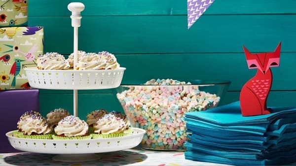 Mesa decorada para una fiesta con cupcakes en un soporte de dos pisos, un bol de nubes de colores y servilletas azules. A un lado destaca una figura roja de papel en forma de zorro.