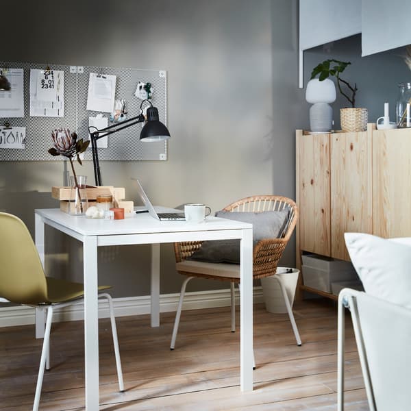 Mesa em branco com um candeeiro de secretária fixado e acessórios de escritório espalhados. Ao lado da mesa está um conjunto de armários IVAR.