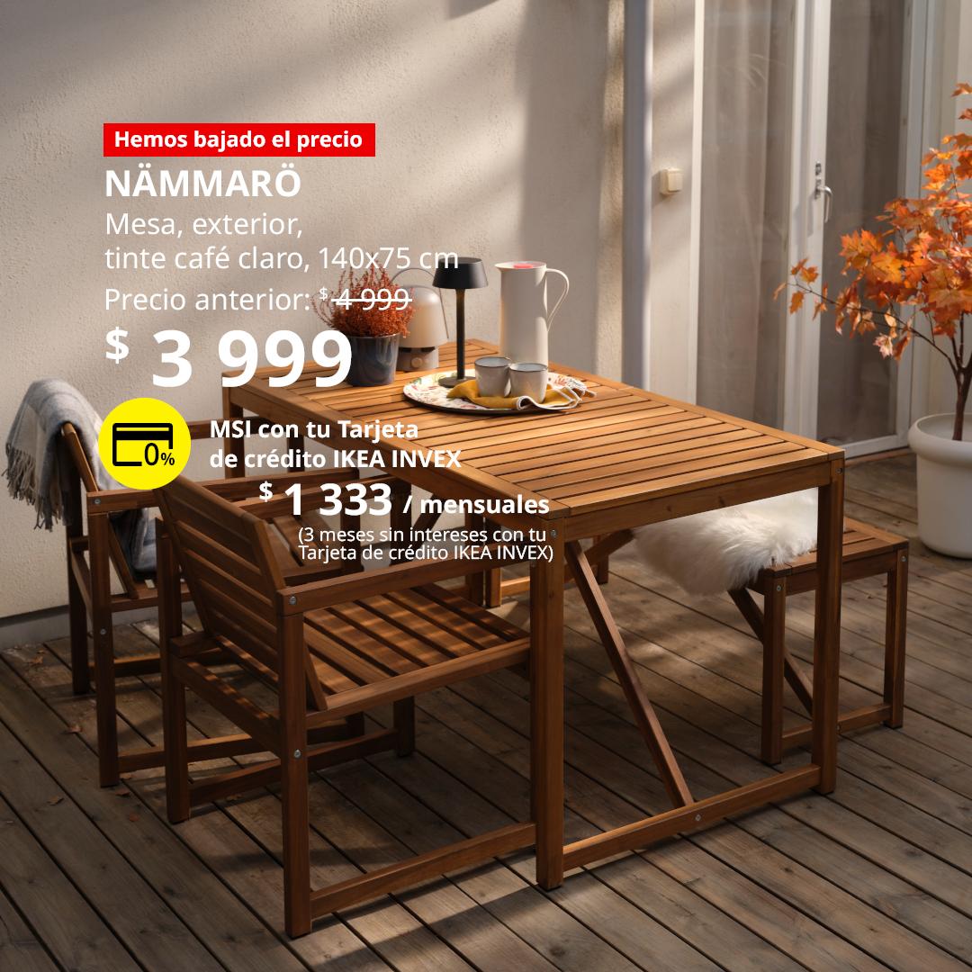 Mesa NÄMMARÖ para exterior en tinte café claro, acompañada de sillas con reposabrazos y una banca en una terraza.