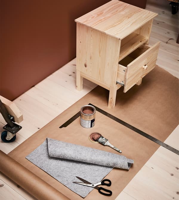 Mesa que espera ser pintada con brocha cunha lata de pintura marrón e cun caixón forrado de feltro para ser engadido.