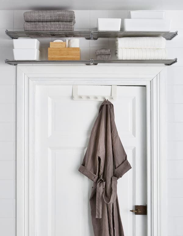 Metal shelves placed above a door frame and store towels and other extras, while a bathrobe hangs from a door hanger.