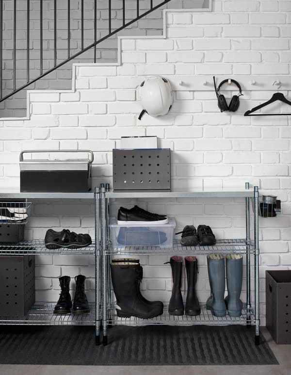 Metal shelving is placed above a doormat to store shoes and several pairs of boots. Storage boxes sit on the top shelf. 