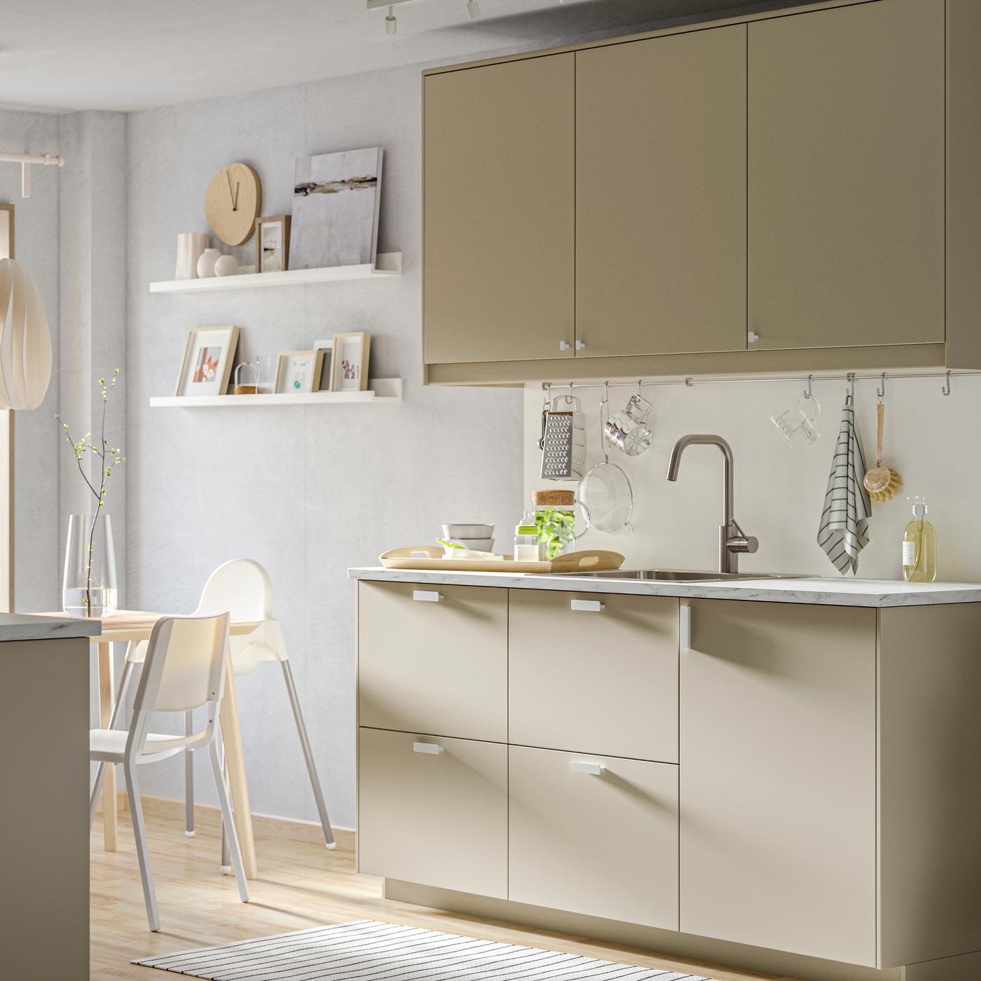 METOD complete kitchen system with HAVSTORP beige kitchen cabinet doors. A dining table with ANTILOP baby chair is placed next to the open kitchen. 