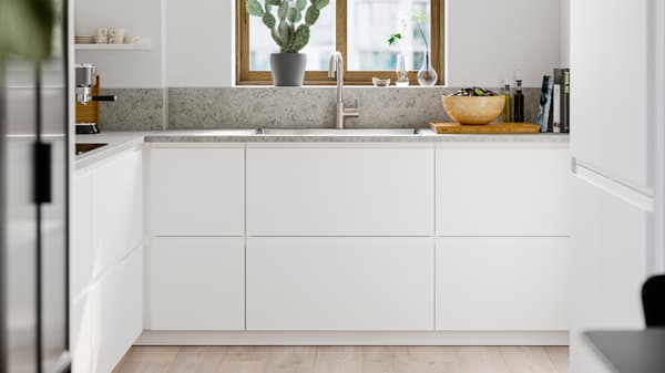 METOD kitchen with handleless cabinets, stone countertop, sink under a window, light wood floor and a decorative cactus on the sill.