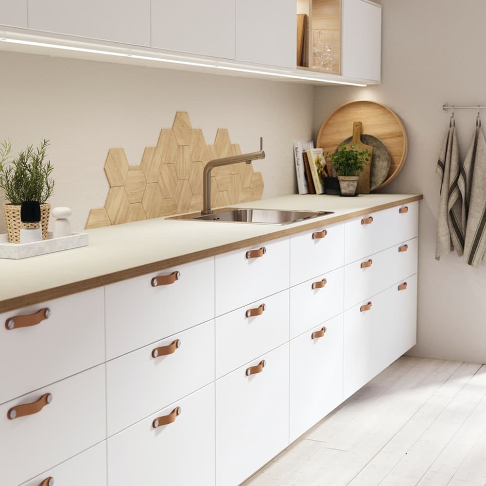 Meuble bas de cuisine blancs avec beaucoup de tiroirs et des poignées en cuir.
