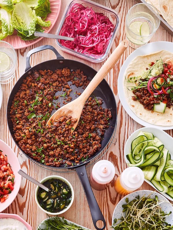 Mexická zmes z bezmäsitého mletého VÄRLDSKLOK na panvici, okolo ležia misky so zeleninou a tanier s tortillou naplnenou bezmäsitou zmesou. 