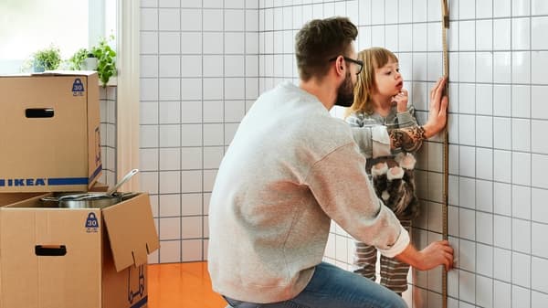 Mężczyzna mierzy ścianę w pomieszczeniu. W tle stoją pudełka IKEA.