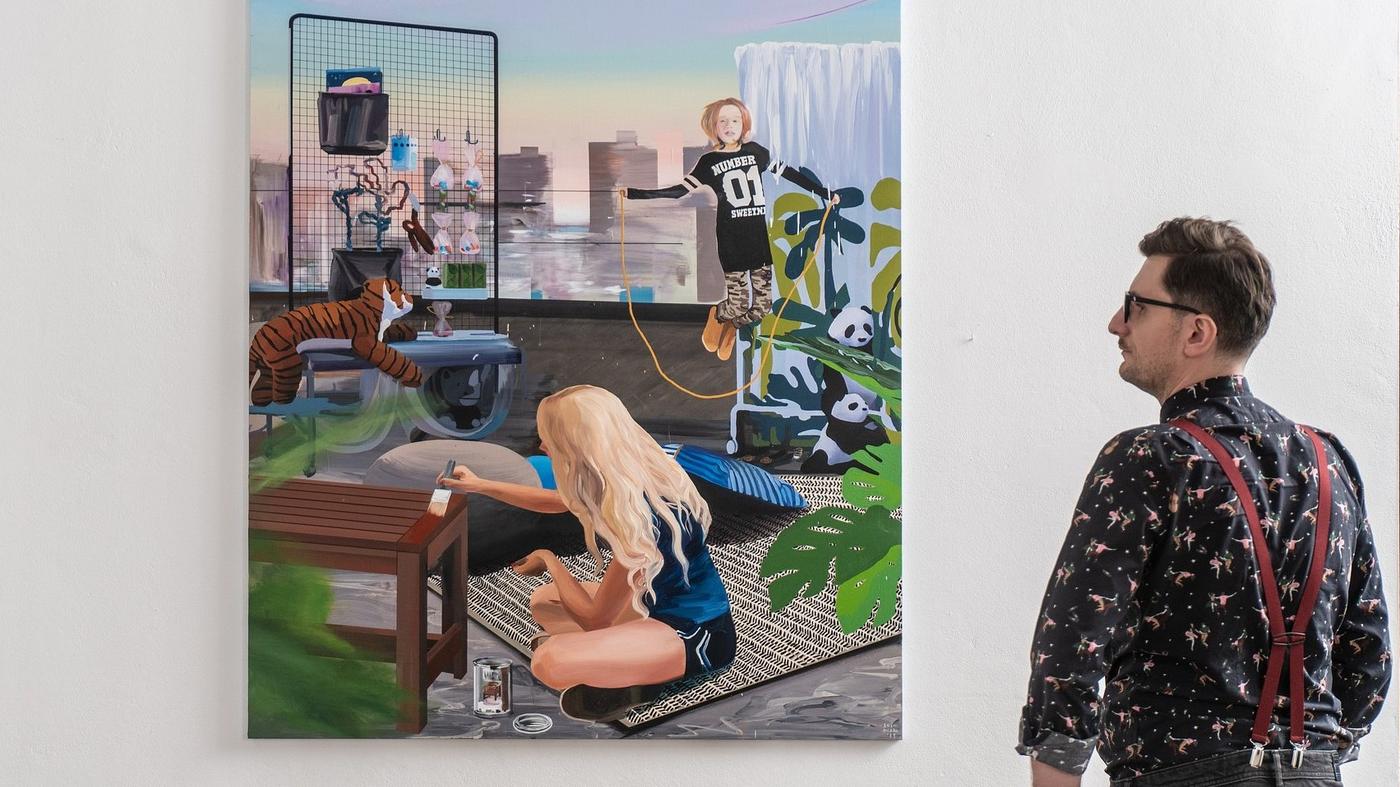 mężczyzna patrzy na obraz, na którym kobieta siedząca na tarasie maluje stół