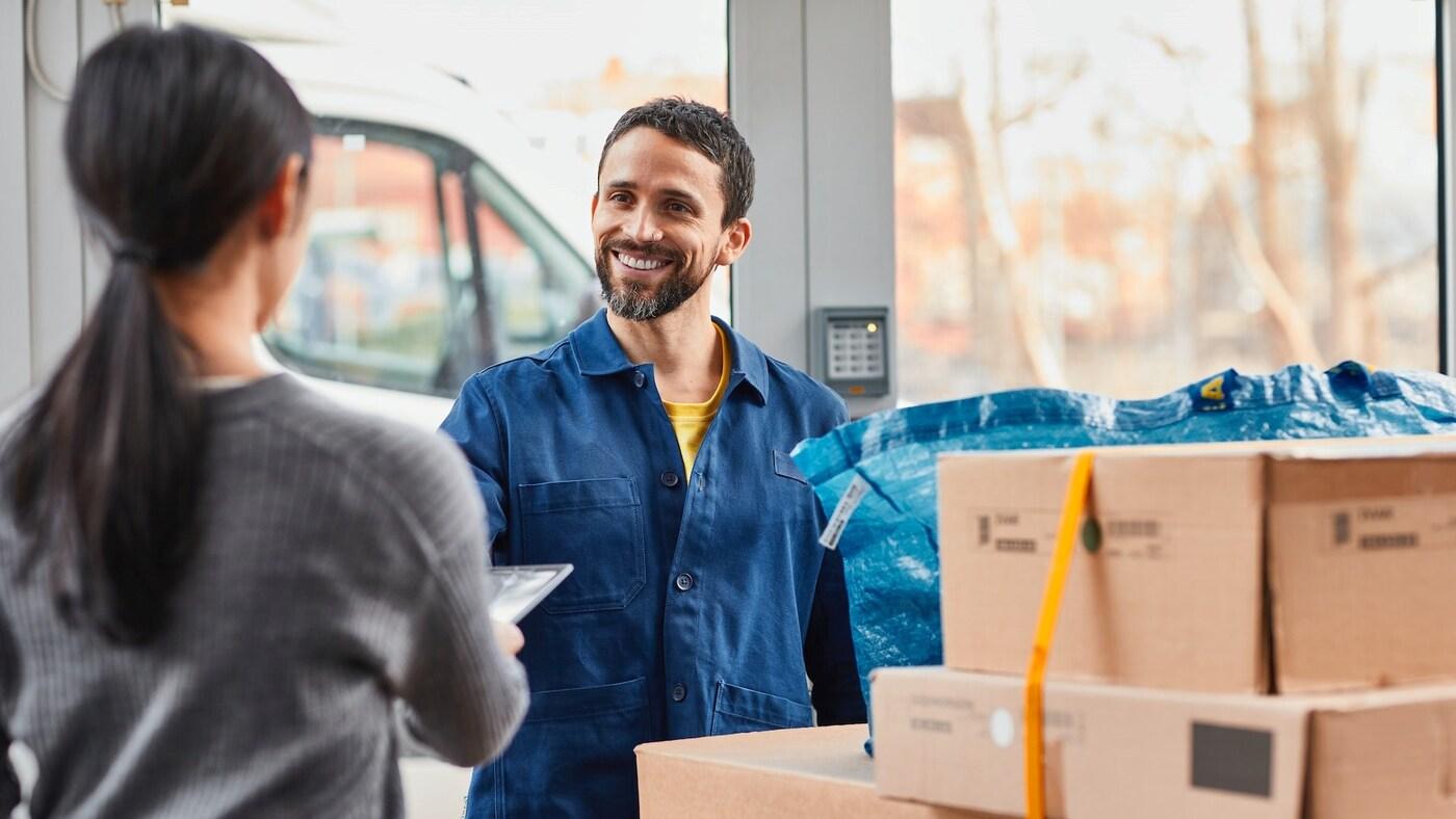  Mężczyzna w niebieskiej kurtce uśmiecha się, obok stoją kartony.
