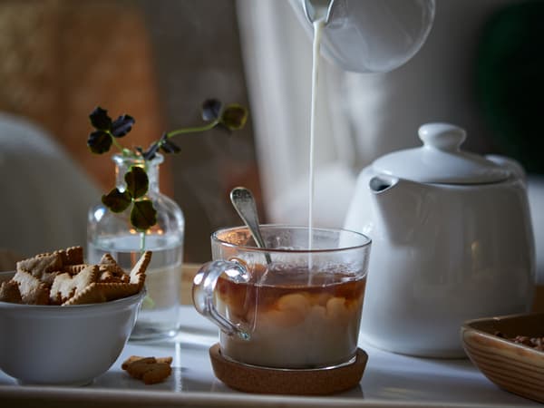 Milch wird in eine Tasse Tee gegossen. Daneben stehen Plätzchen und eine weisse Teekanne