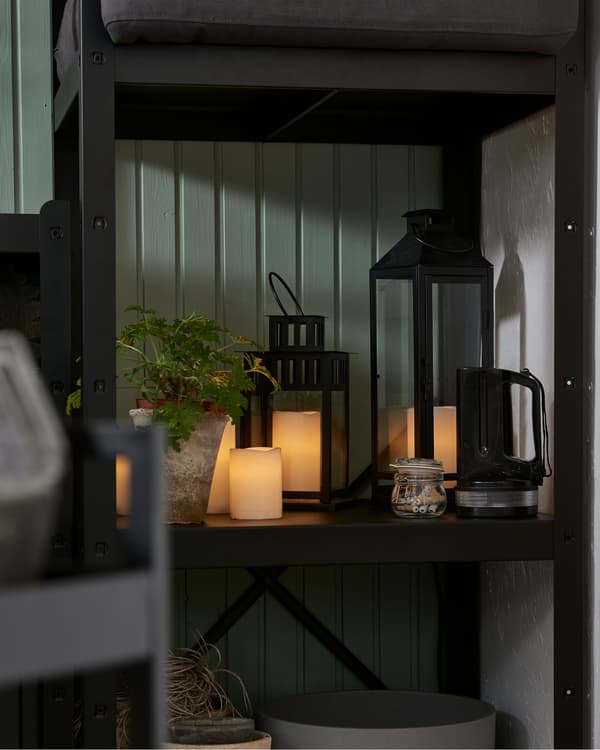Milieu d’une étagère dans le coin de la pièce, avec une série de bougies LED et une plante.