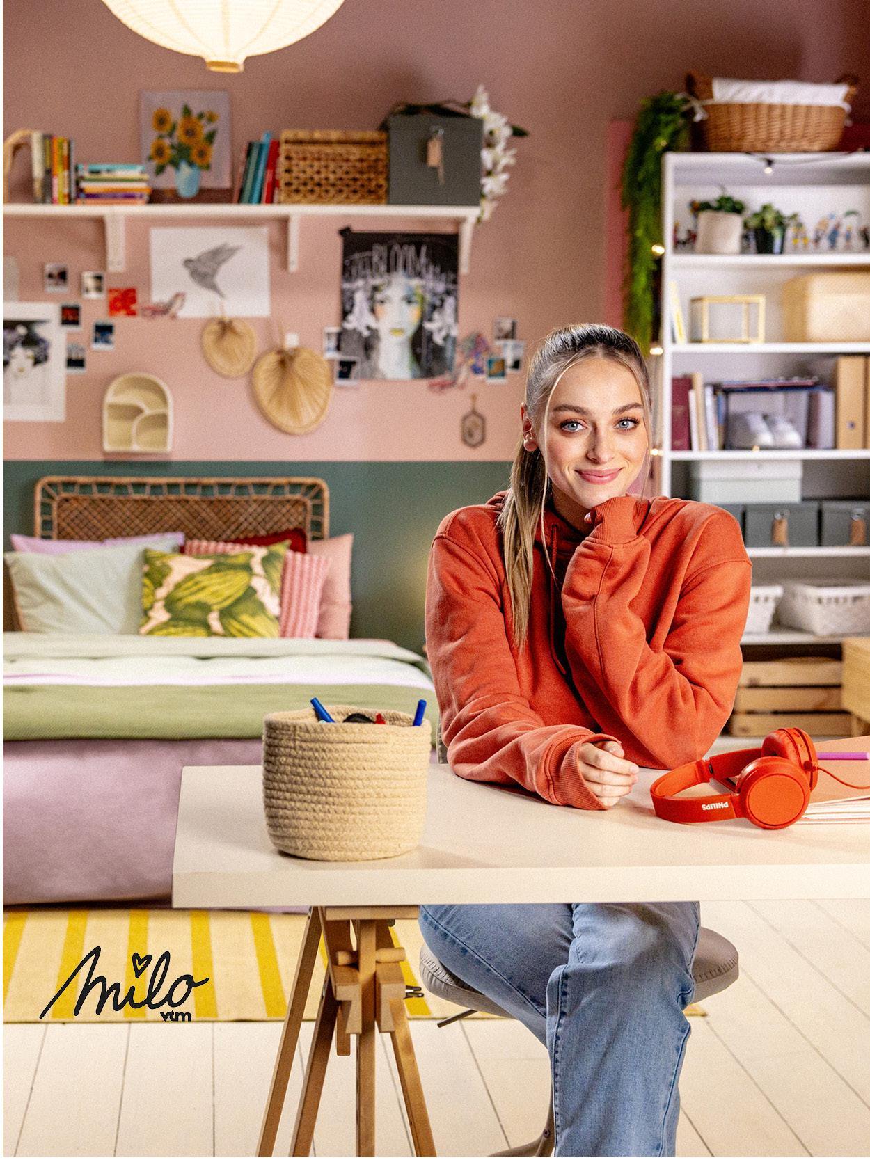 Milo est assis à une table IKEA dans une pièce colorée avec des plantes et des décorations, avec un casque.