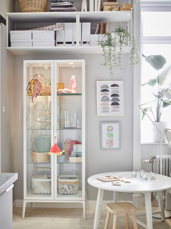 ตู้ MILSBO/มีลสบู สูงสีขาวเก็บของโชว์ได้ ตั้งอยู่ตรงมุมใต้ชั้นวางแขวนผนังด้านบนที่เก็บของได้มาก