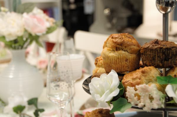 Mini muffin salati al salmone affumicato messi su un'alzata. Accanto, alcuni bicchieri e fiori sparsi.