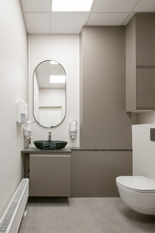 Minimalist bathroom with wall-mounted toilet, oval mirror, modern sink, and neutral cabinetry.