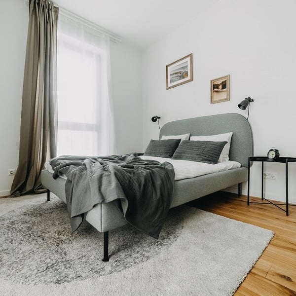 Minimalist bedroom with grey upholstered bed, matching bedding, and wall-mounted reading lamps.