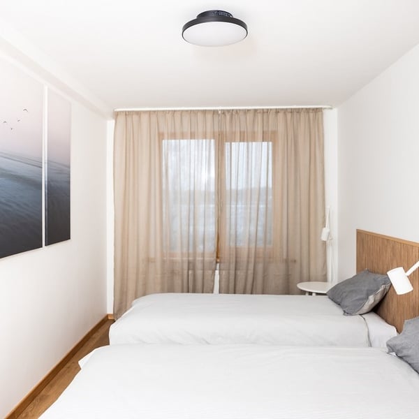 Minimalist bedroom with two single beds, gray pillows, and beige curtains.