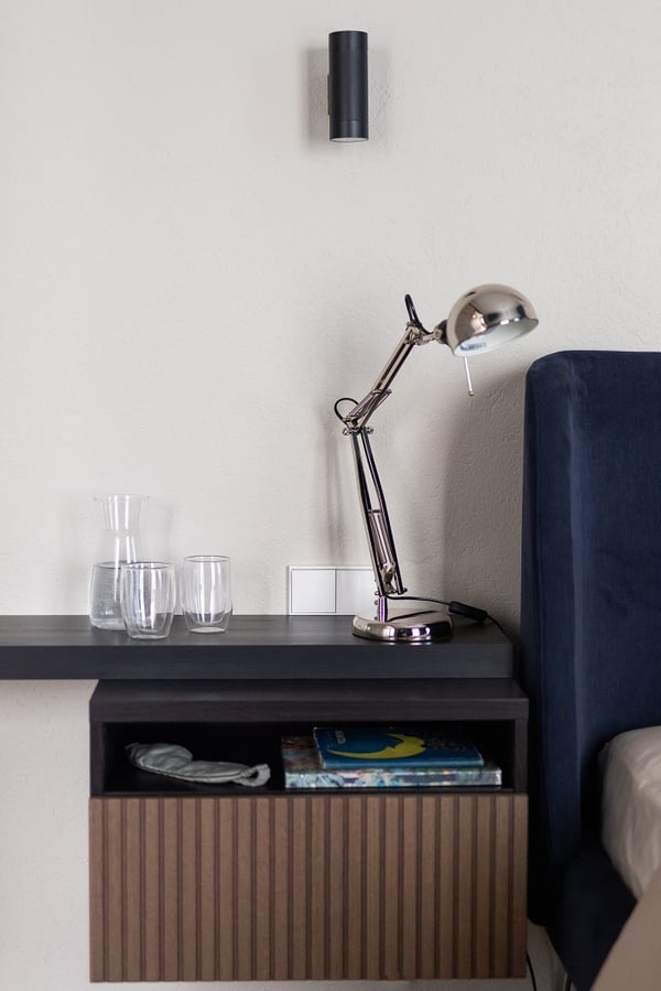 Minimalist bedside table with reading lamp, glasses, and bedroom decor details