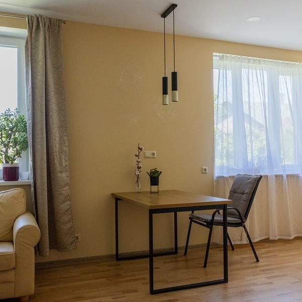 Minimalist dining area with wooden table, black metal legs and pendant lighting near a window
