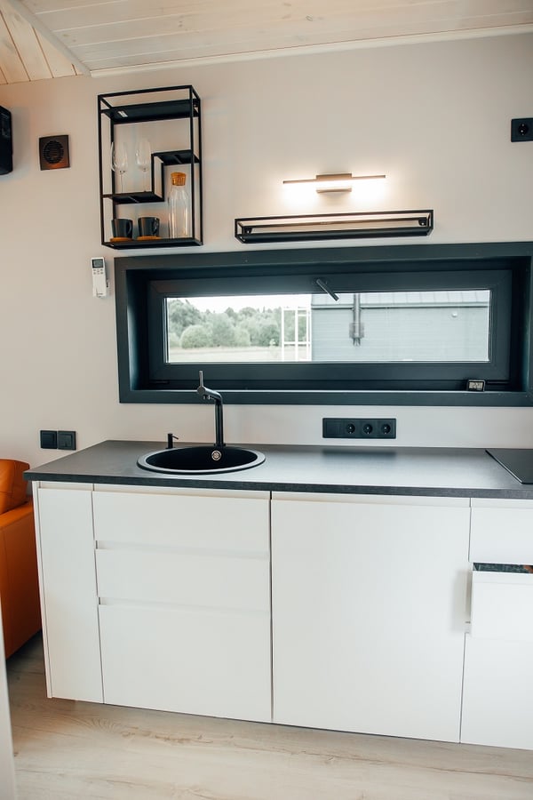 Minimalist kitchen with black round sink and white cabinets – Compact modern kitchen featuring sleek white cabinetry, black countertop, and wall-mounted shelves with glassware.