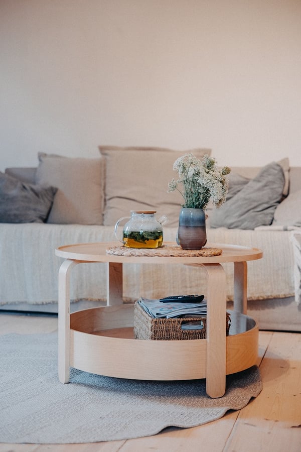 Minimalist round wooden coffee table with flowers in a vase and herbal tea in a glass teapot.