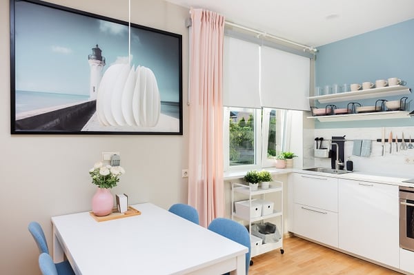 Минималистичная обеденная зона с белым столом, синими стульями и подвесным светильником рядом с кухней
