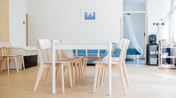 Minimalistická jídelna s dřevěným stolem a židlemi, s výhledem na modrou pohovku. Světlý interiér, moderní nábytek, obývací prostor, jídelní kout.