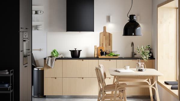 Minimalistická kuchyně se světlými bambusovými čely zásuvek, černými dvířky, světlým bambusovým jídelním stolem a dvěma židlemi.