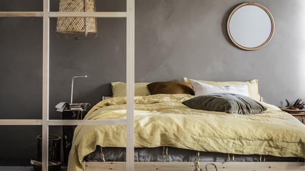 Minimalistisk soveværelse med grå vægge og et afdæmpet farvetema, detaljer af træ, en NEIDEN dobbeltseng og en KNIXHULT lampe.