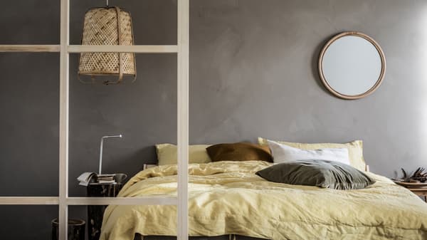 Minimalistisk soveværelse med grå vægge og et afdæmpet farvetema, detaljer af træ, en NEIDEN dobbeltseng og en KNIXHULT lampe.
