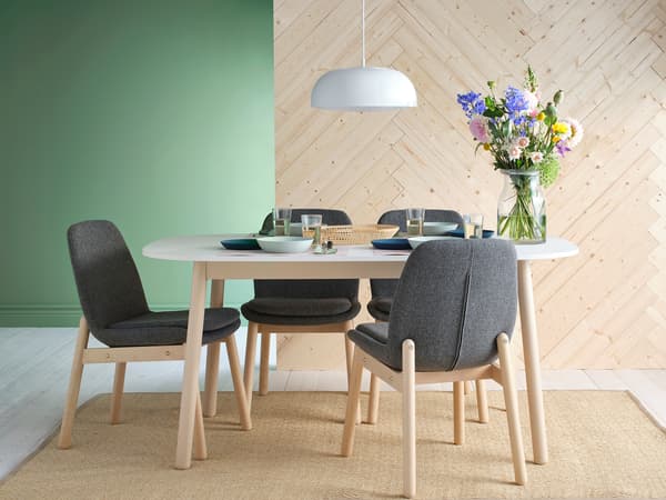 丸みのある白いテーブルにグレーのチェアを合わせたモダンダイニング。緑の壁と花で彩りをプラス。