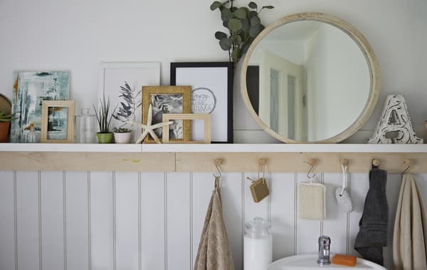 Miroir, plantes, illustrations et coquillages sur une tablette de salle de bain placée au-dessus de crochets.